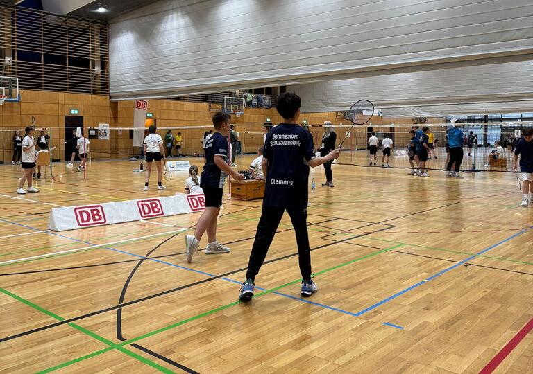 Zentral stehen zwei Badmintonspieler im dunkelblauen Trikot des Gymnasiums