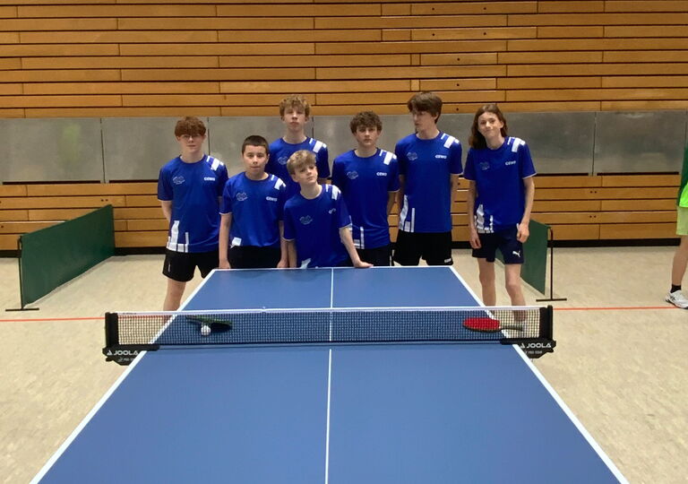 Sieben Schüler im blauen Trikot stehen hinter einer Tischtennisplatte. Es ist das Mannschaftsfoto.