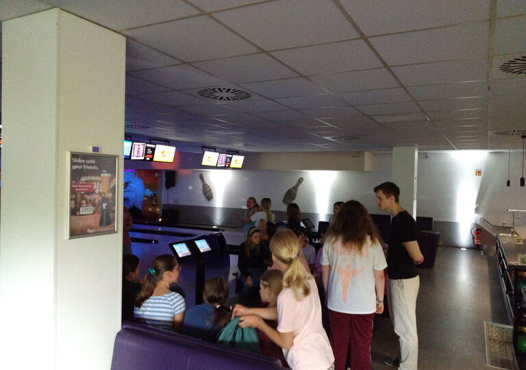 Schüler sitzen auf den Bänken hinter der Bowlingbahn und warten auf ihren nächsten Wurf