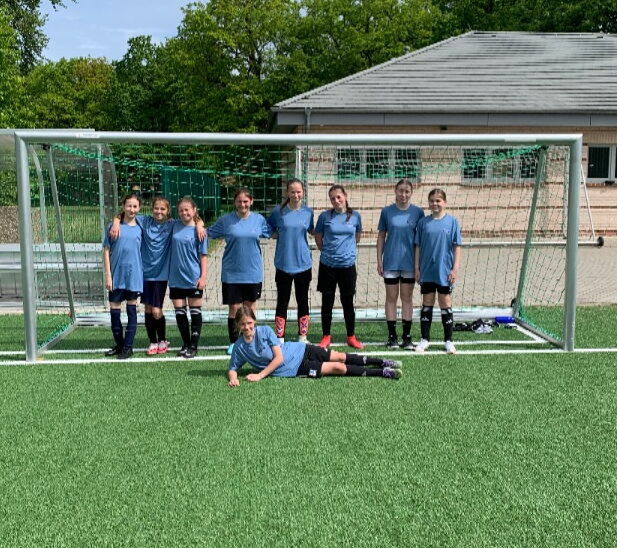 Foto der U15-Fußballmannschaft der Mädchen, acht Mädchen im hellblauen Trikot stehen im Fußballtor, ein weiteres Mädchen liegt davor.