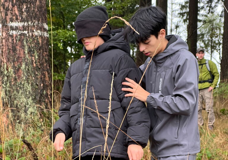 Ein Schüler führt einen anderen Schüler mit verbundenen Augen durch den Wald