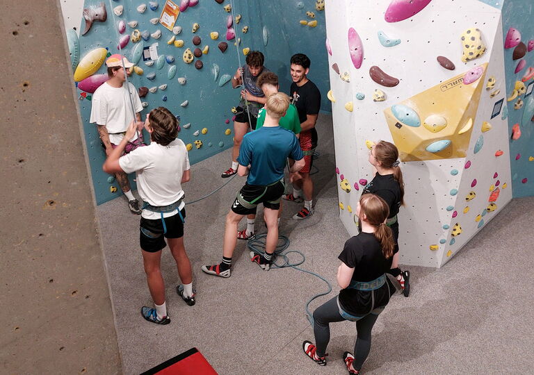 Eine Schülergruppe steht vor einer Kletterwand