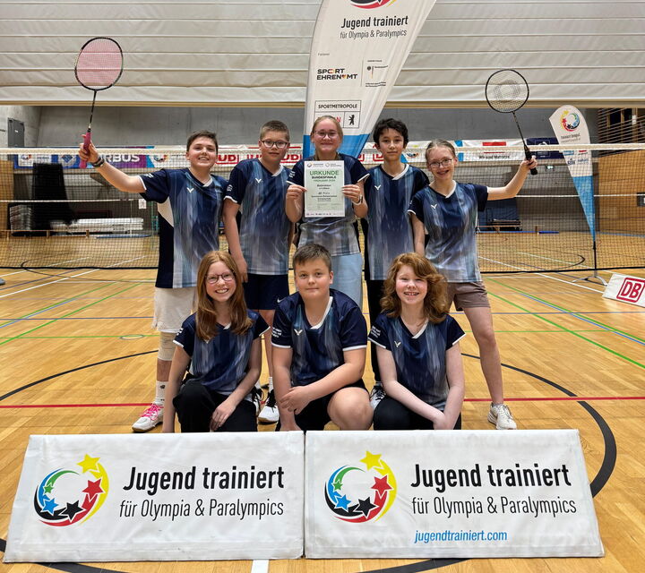 Acht Spielerinnen und Spieler der Badminton-Mannschaft mit Urkunde in der Hand, sitzend und stehend hinter dem Banner von "Jugend trainiert für Olympia"