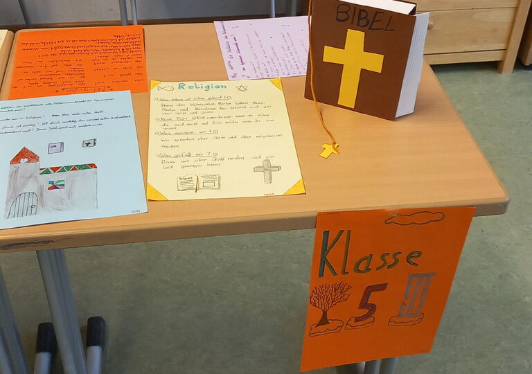 Tisch mit einer Bibel und handgeschriebenen Plakaten zum Thema Religion