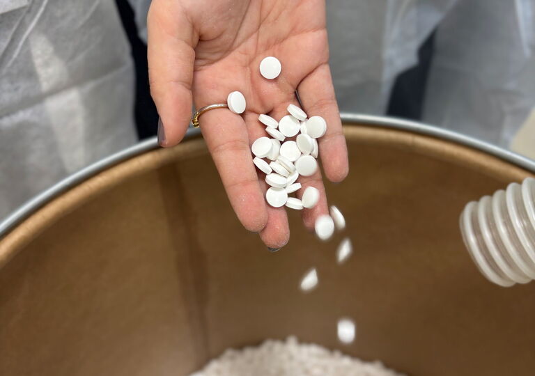 Von einer Hand fällt weißes Granulat in einen großen Topf