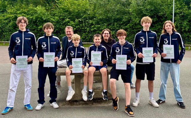 Sieben Schüler der U18-Tischtennis-Mannschaft präsentieren ihre Urkunden, die sie von Bürgermeister Norbert Lütjens und Schulleiterin Kristin Krause erhalten haben.