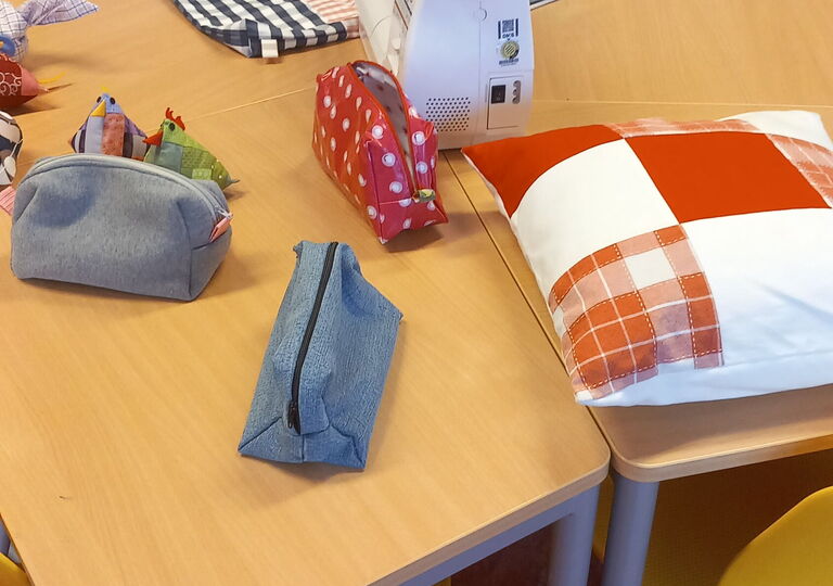 Nähmaschine mit drei bunten Federtaschen und einem rot-weißen Kissen