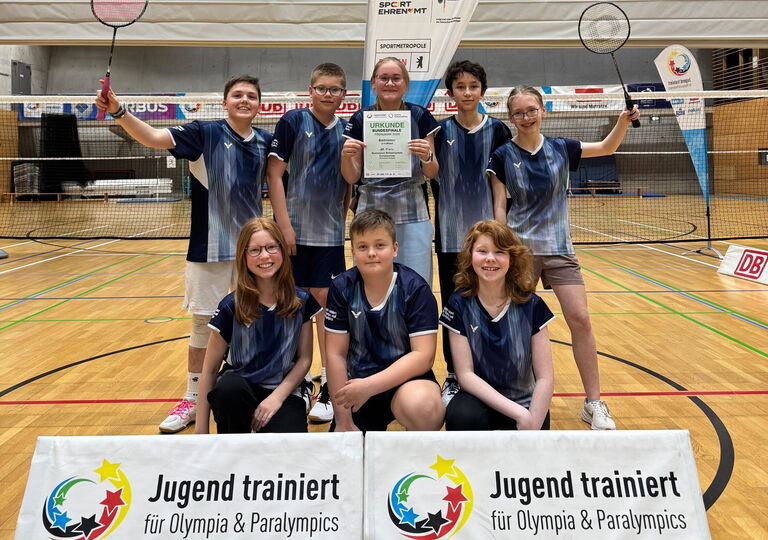 Acht Spielerinnen und Spieler der Badminton-Mannschaft mit Urkunde in der Hand, sitzend und stehend hinter dem Banner von "Jugend trainiert für Olympia"