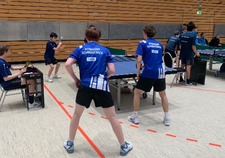 Zwei Spieler in blauen Trikots spielen ein Match gegen zwei weitere Spieler