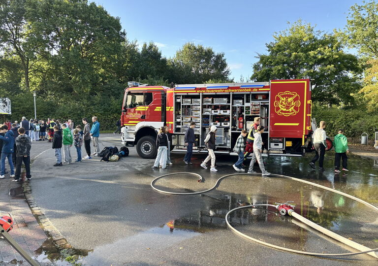 Bild eines Feuerwehrschlauchs und im Hintergrund ein offenes Feuerwehrauto