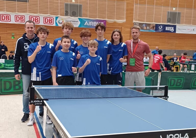 Sieben Tischtennisspieler und ihre beiden Lehrer stehen für ein Gruppenfoto hinter einer Tischtennisplatte
