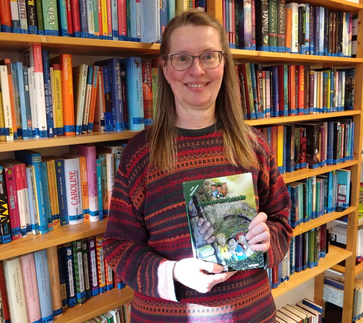 Frau Brauer mit einem Buch in der Hand vor einem Bücherregal stehend