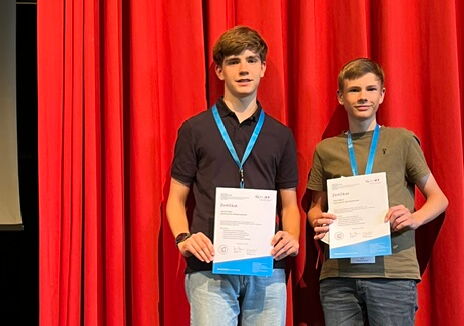 Jannik und Felix stehen vor einem roten Vorhang und halten ihre Urkunde in der Hand