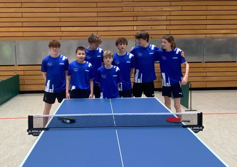 Sieben Schüler im blauen Trikot stehen hinter einer Tischtennisplatte. Es ist das Mannschaftsfoto.