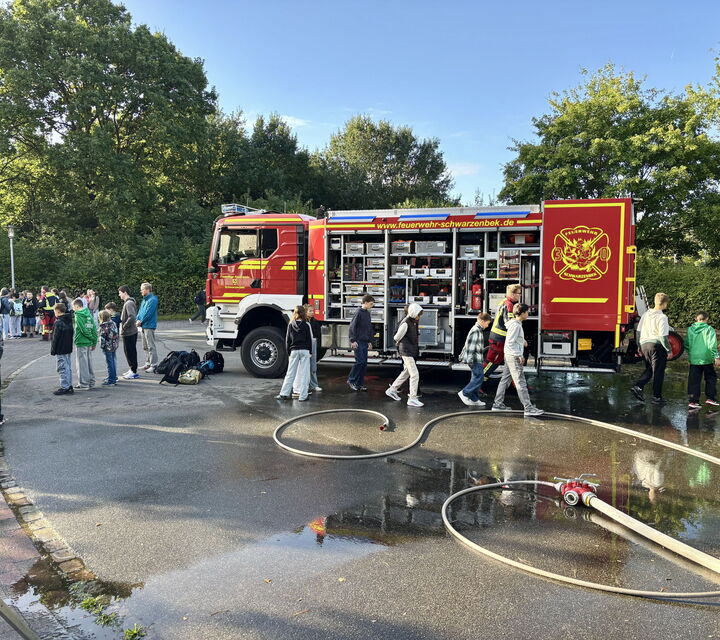Bild eines Feuerwehrschlauchs und im Hintergrund ein offenes Feuerwehrauto