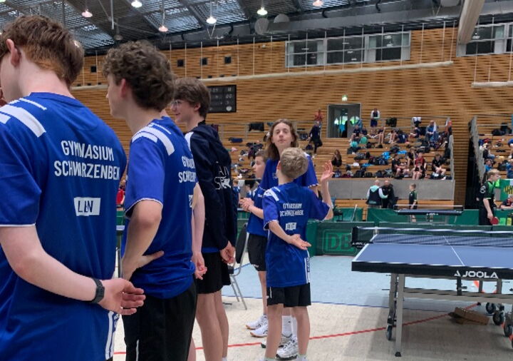 Sechs Schüler der Tischtennismannschaft stehen mit dem Rücken zur Kamera. Man sieht die blauen Trikots des Gymnasiums Schwarzenbek.